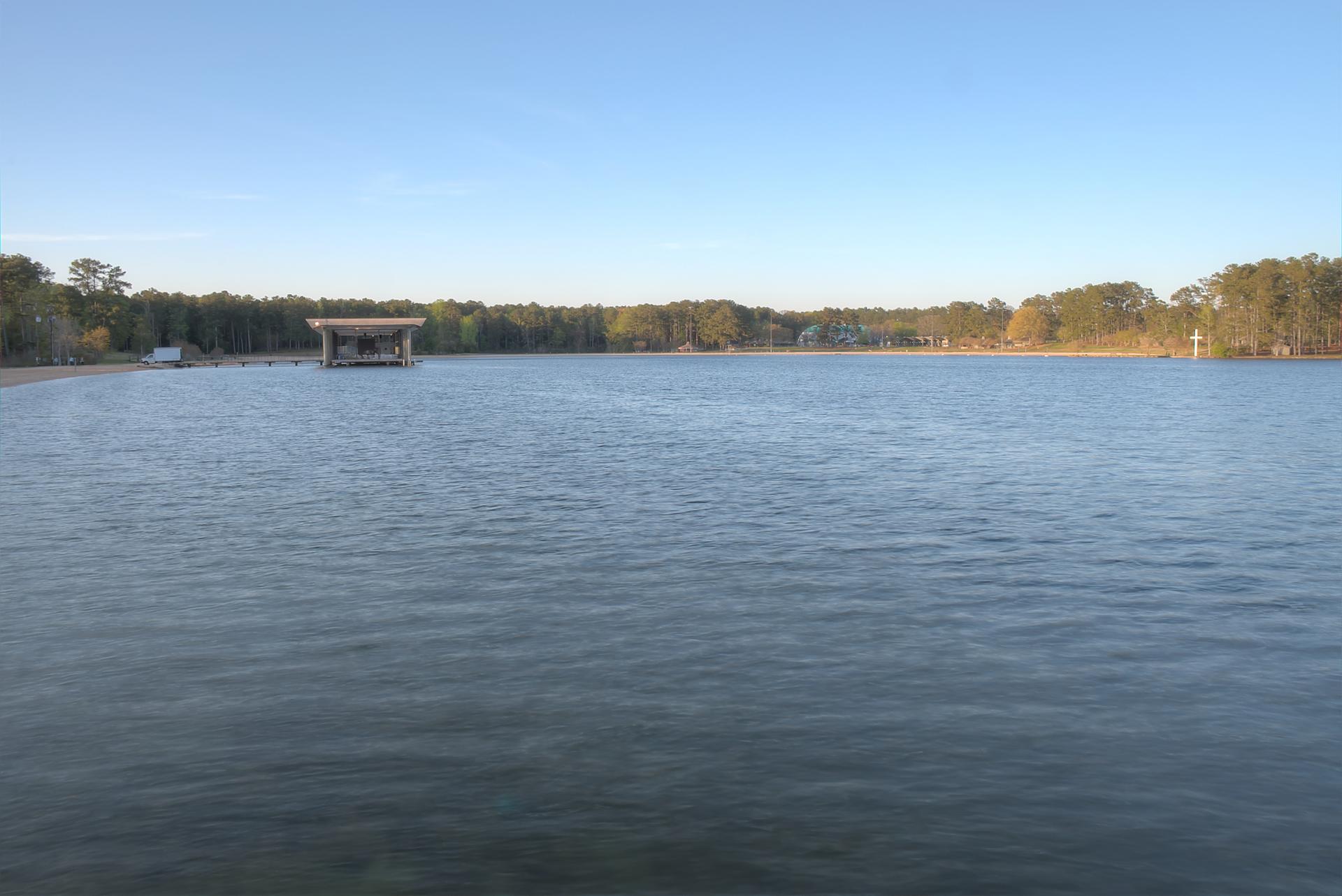 Wide view of a calm lake with a distant dock and forested shore.