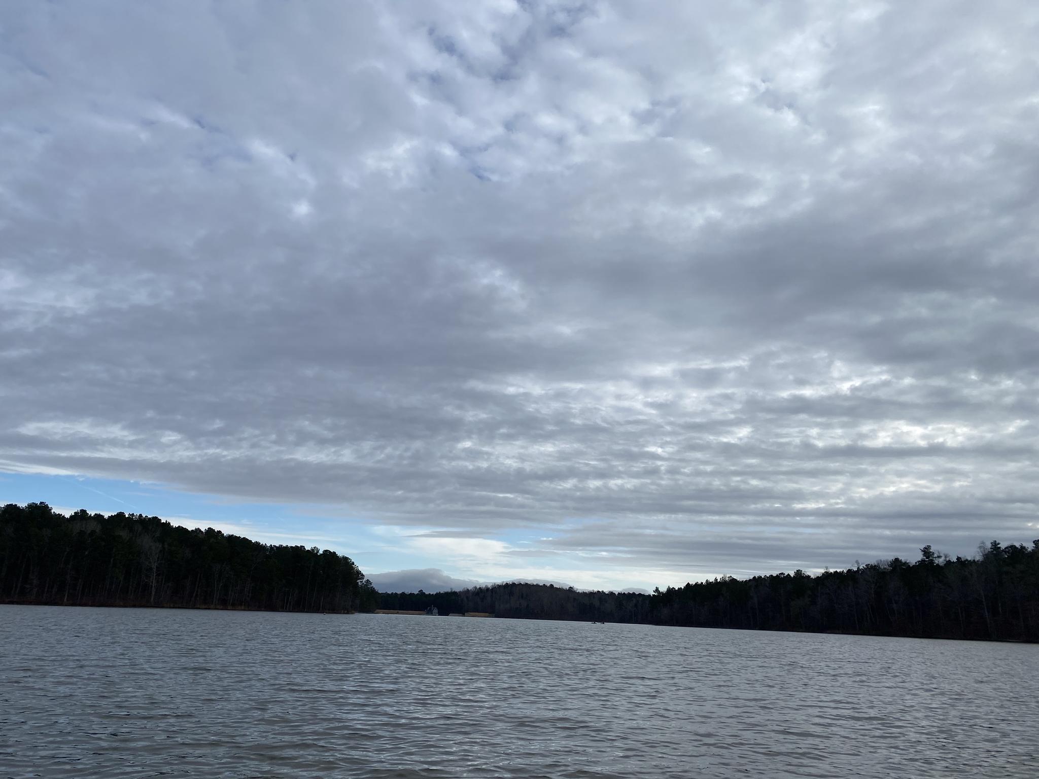 Wide shot of a lake with dark forested shores under an overcast sky.
