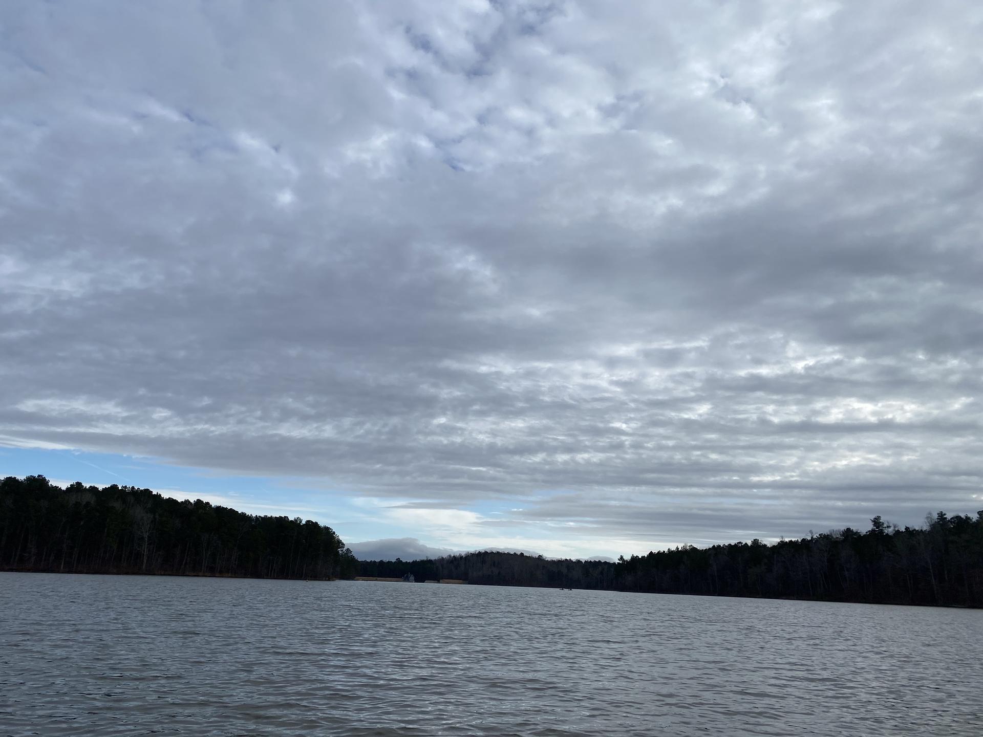 Wide shot of a lake with dark forested shores under an overcast sky.