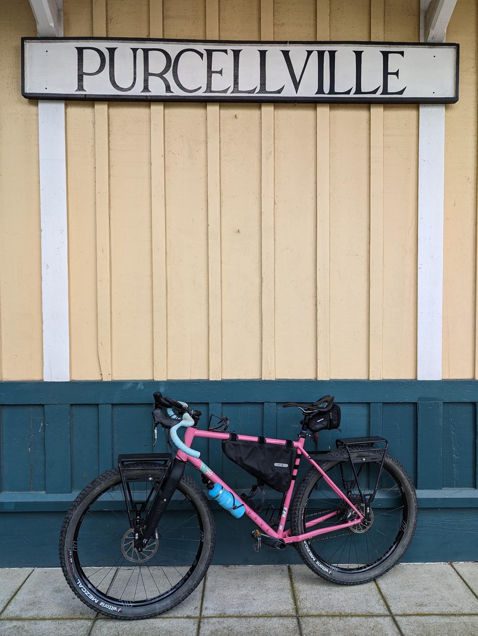 A pink bicycle with gear parked against a yellow and blue building wall.