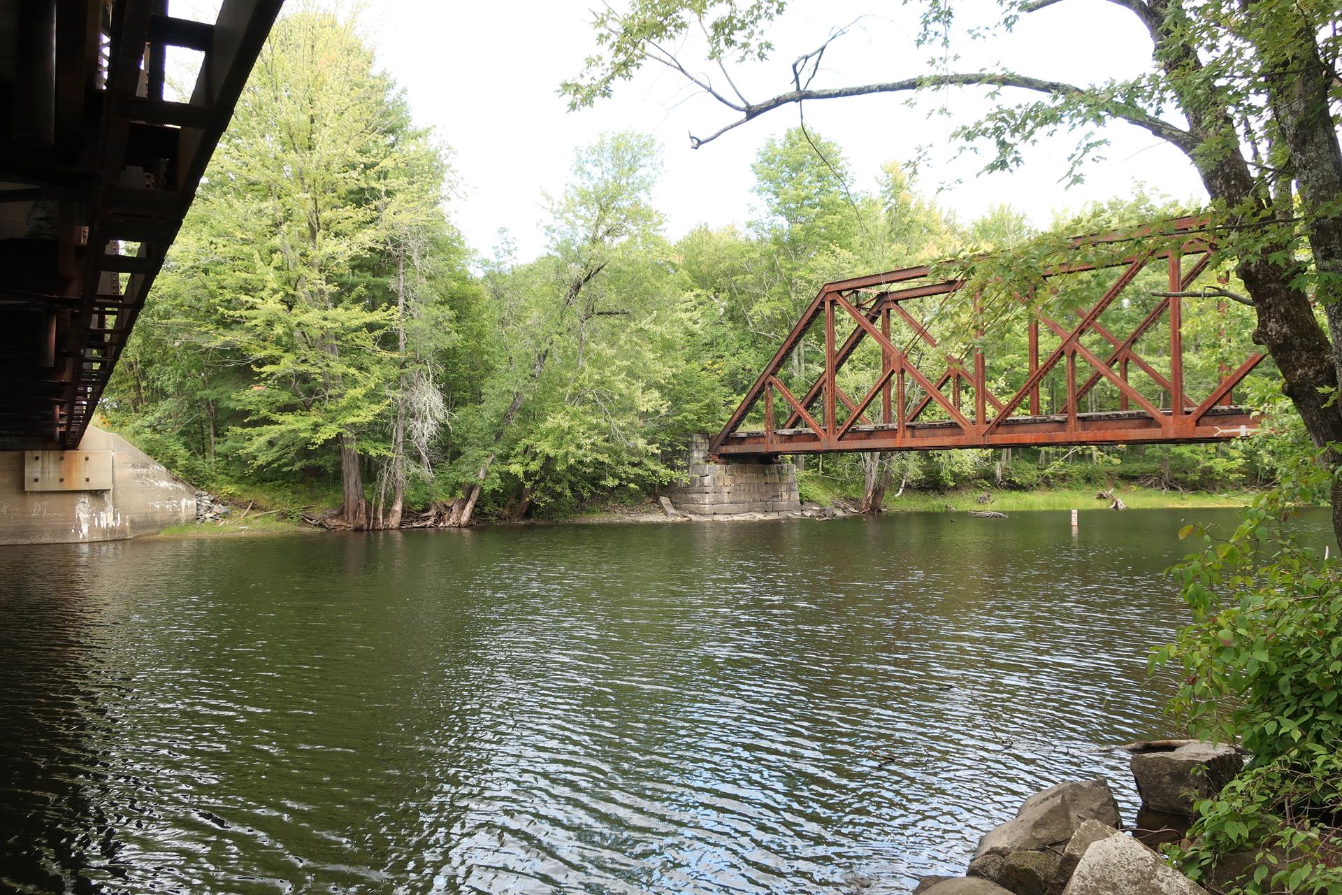 Two bridges spanning a calm river surrounded by lush green trees.