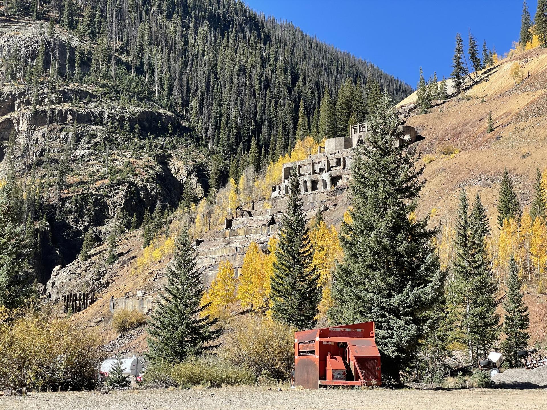Ancient industrial ruins cling to a steep mountain hillside with autumn trees.