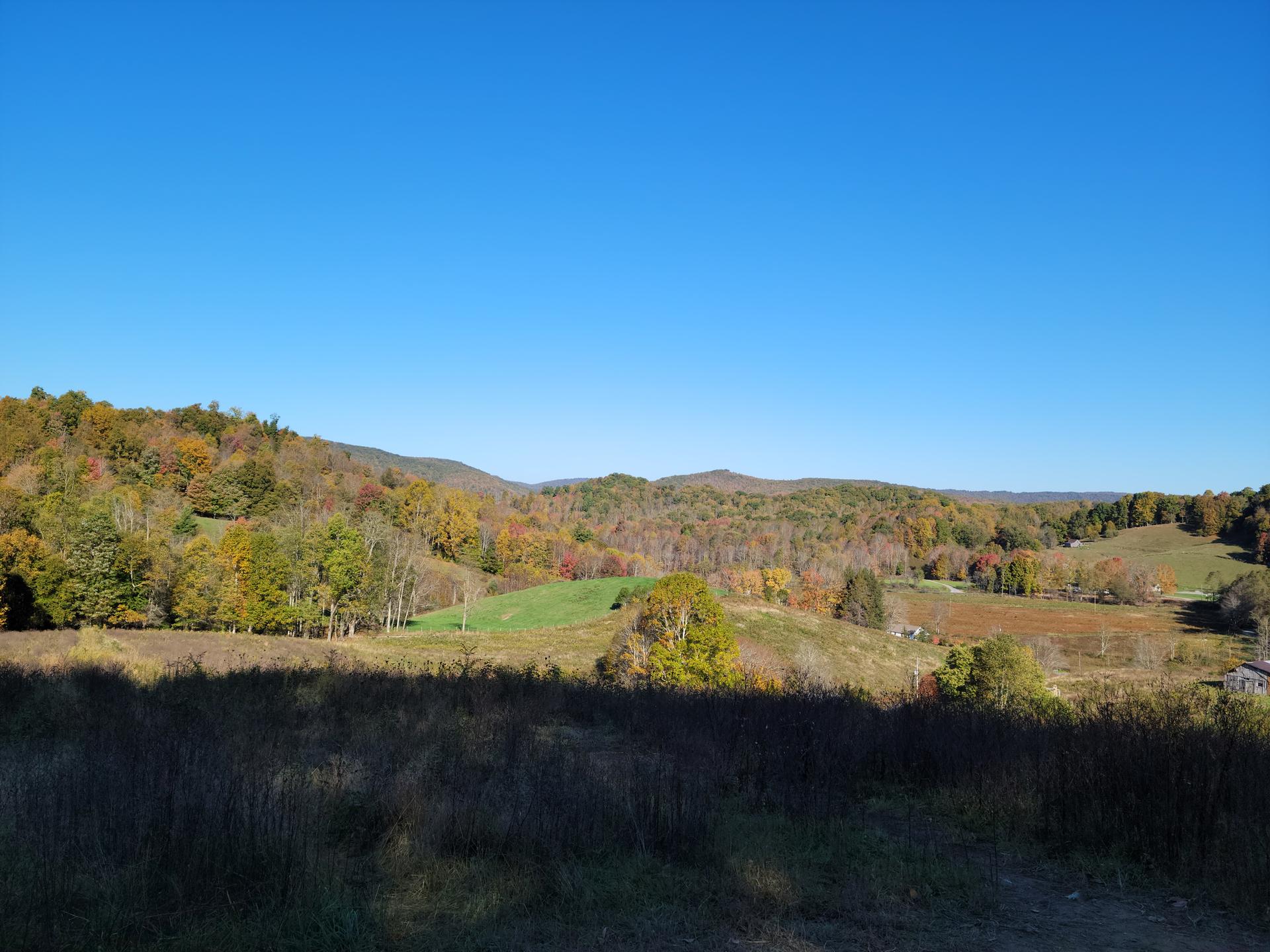 Autumn hillsides with colorful trees and fields under a clear blue sky.