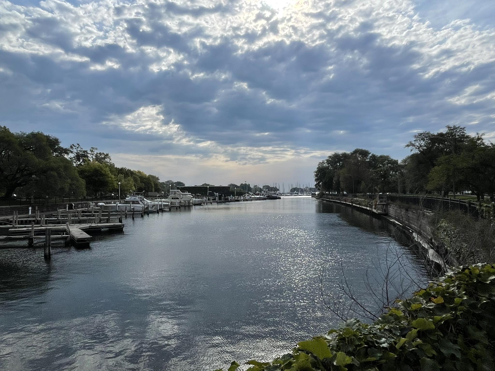 A wide waterway with docks and trees under a bright, cloudy sky.