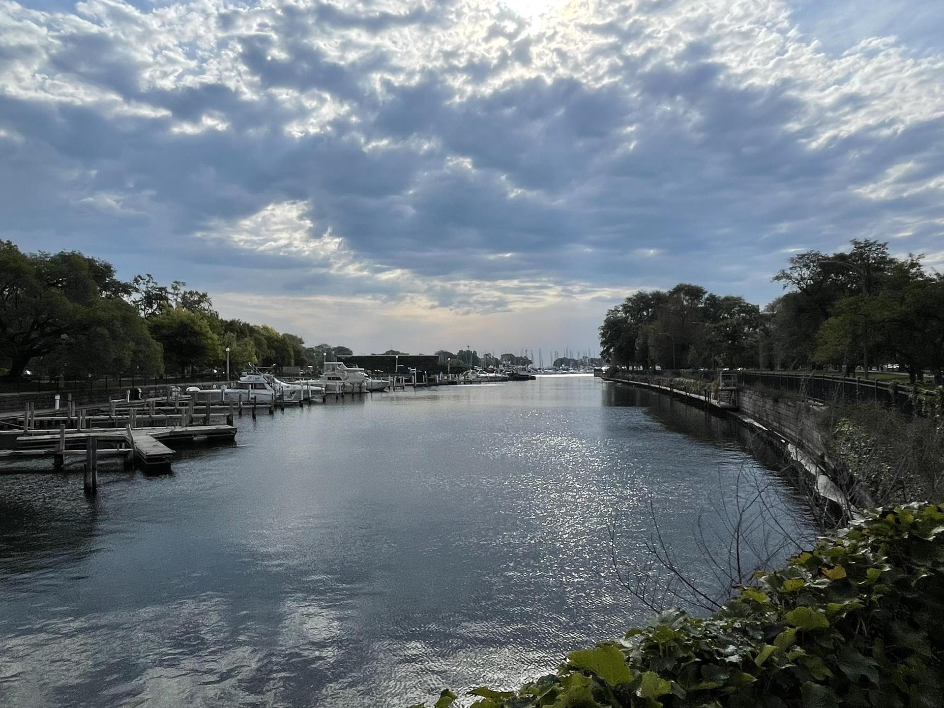 A wide waterway with docks and trees under a bright, cloudy sky.
