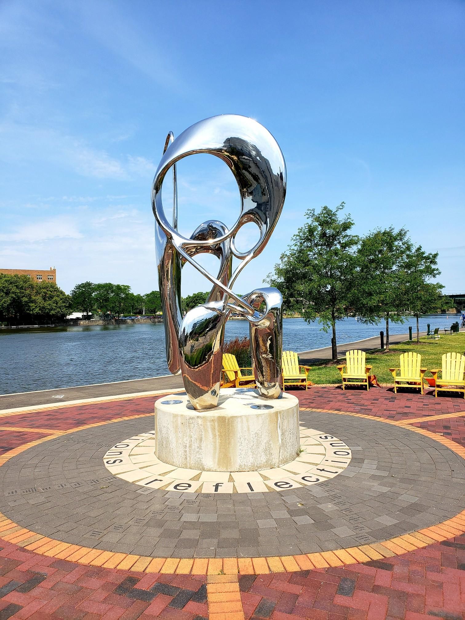 Shiny modern sculpture on a brick plaza by a river on a sunny day. - Fox River Trail (FRT) – Riverside Park (Buie Park) loop from Bartlett