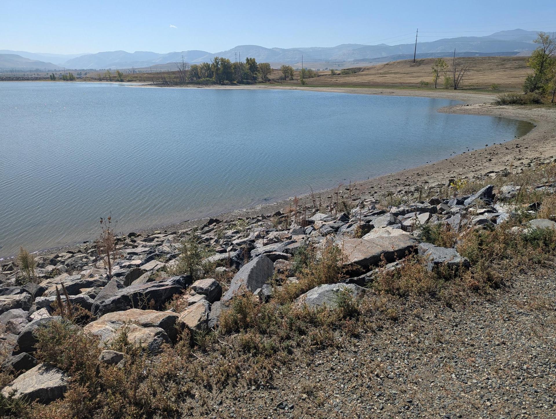 Sunny view of a lake with a rocky shore and distant mountains.