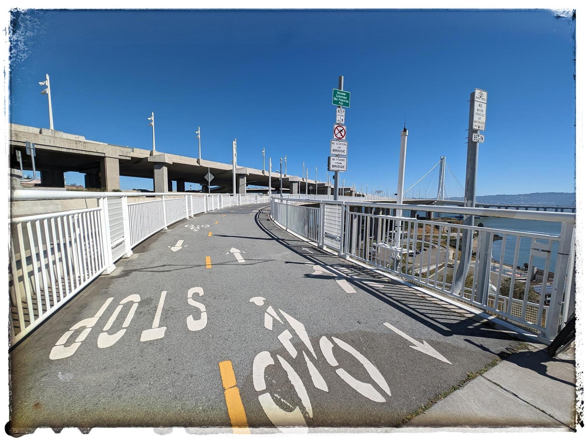 Paved bike path with "STOP" and bike symbols, alongside a bridge.