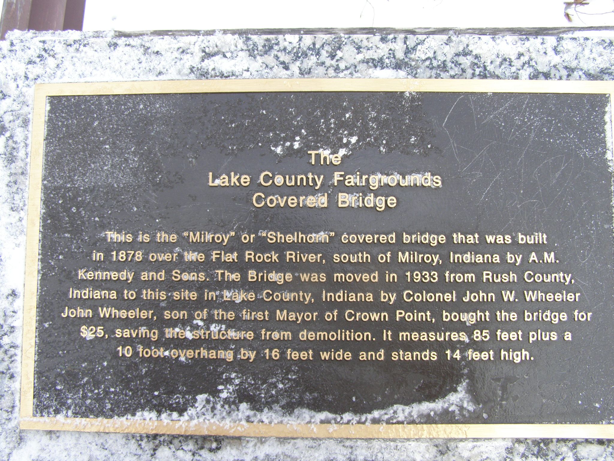 A weathered bronze historical plaque with gold text on a speckled stone base. - Lake County Fairgrounds loop