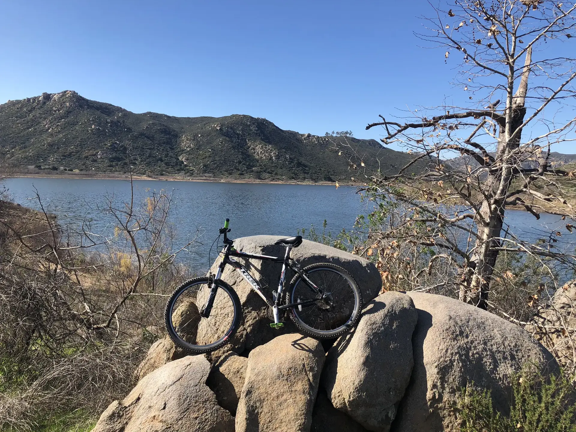 Mountain bike resting on large rocks overlooking a lake and mountains. Bright sun.