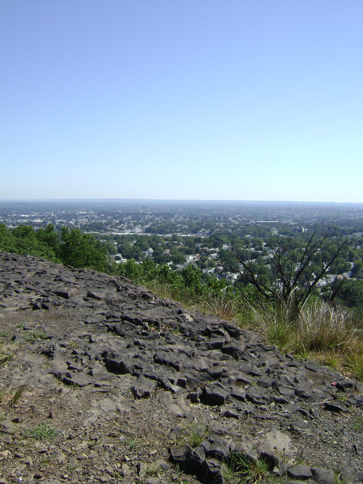 A rocky cliff edge overlooks a sprawling town under a clear blue sky.