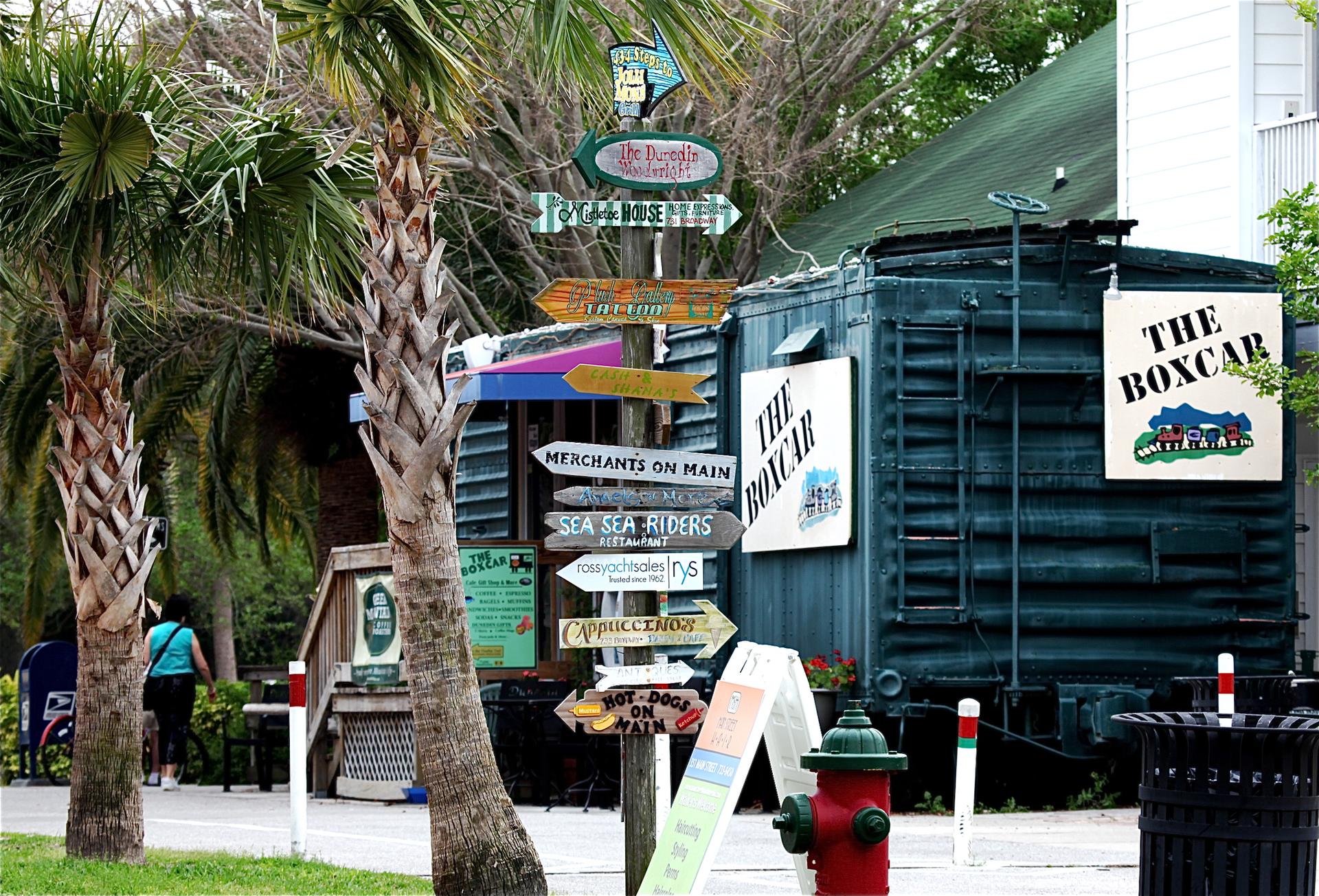 A busy signpost with many directional arrows, palm trees, and a building.