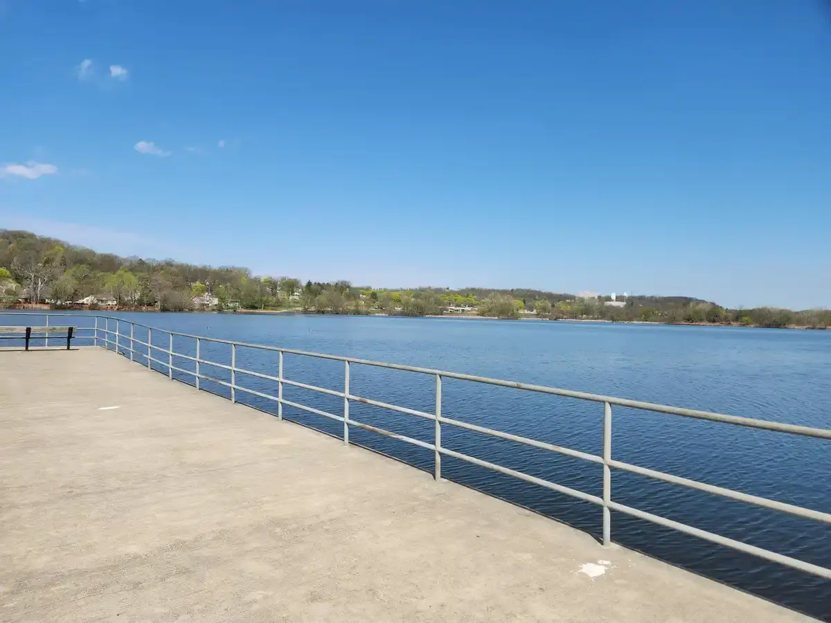 A wide lake view from a concrete pier with a railing on a sunny day.