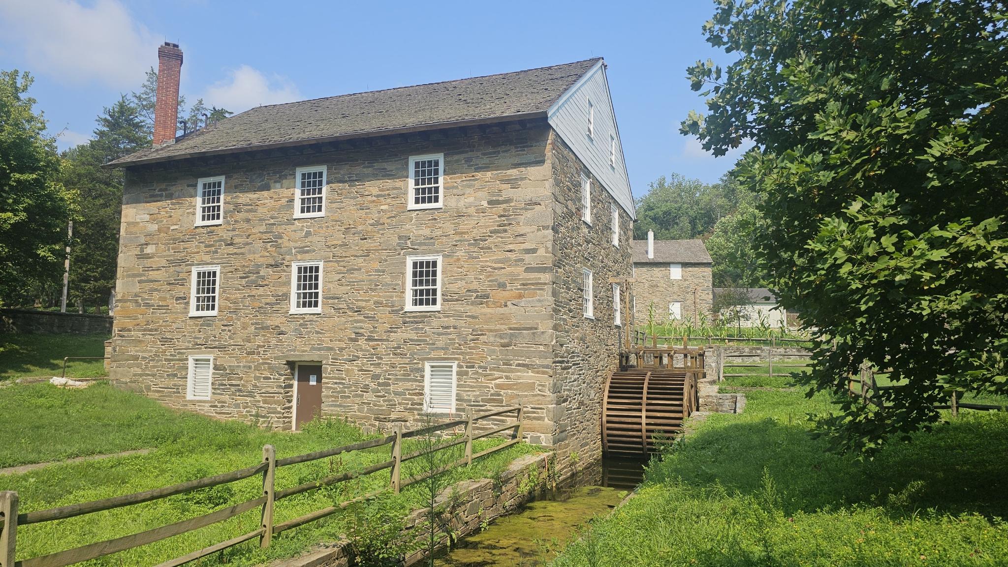 An old stone mill with a water wheel, surrounded by green trees.