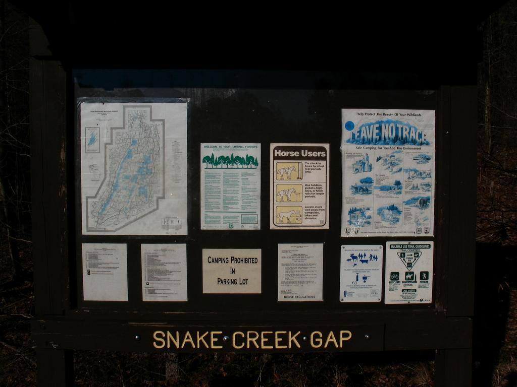 A dark information board with maps and notices in dim outdoor light.