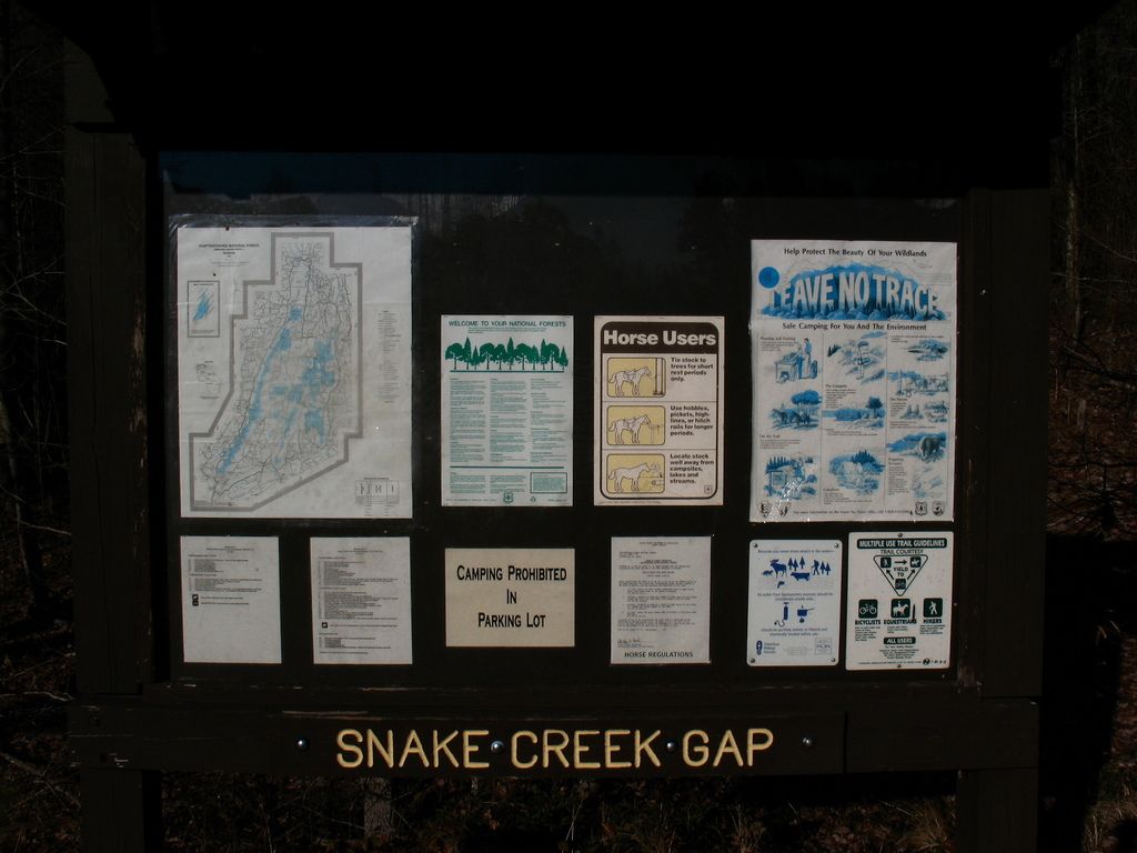 A dark information board with maps and notices in dim outdoor light. - Pinhoti Trail: GA 136 to Mill Creek Mountain
