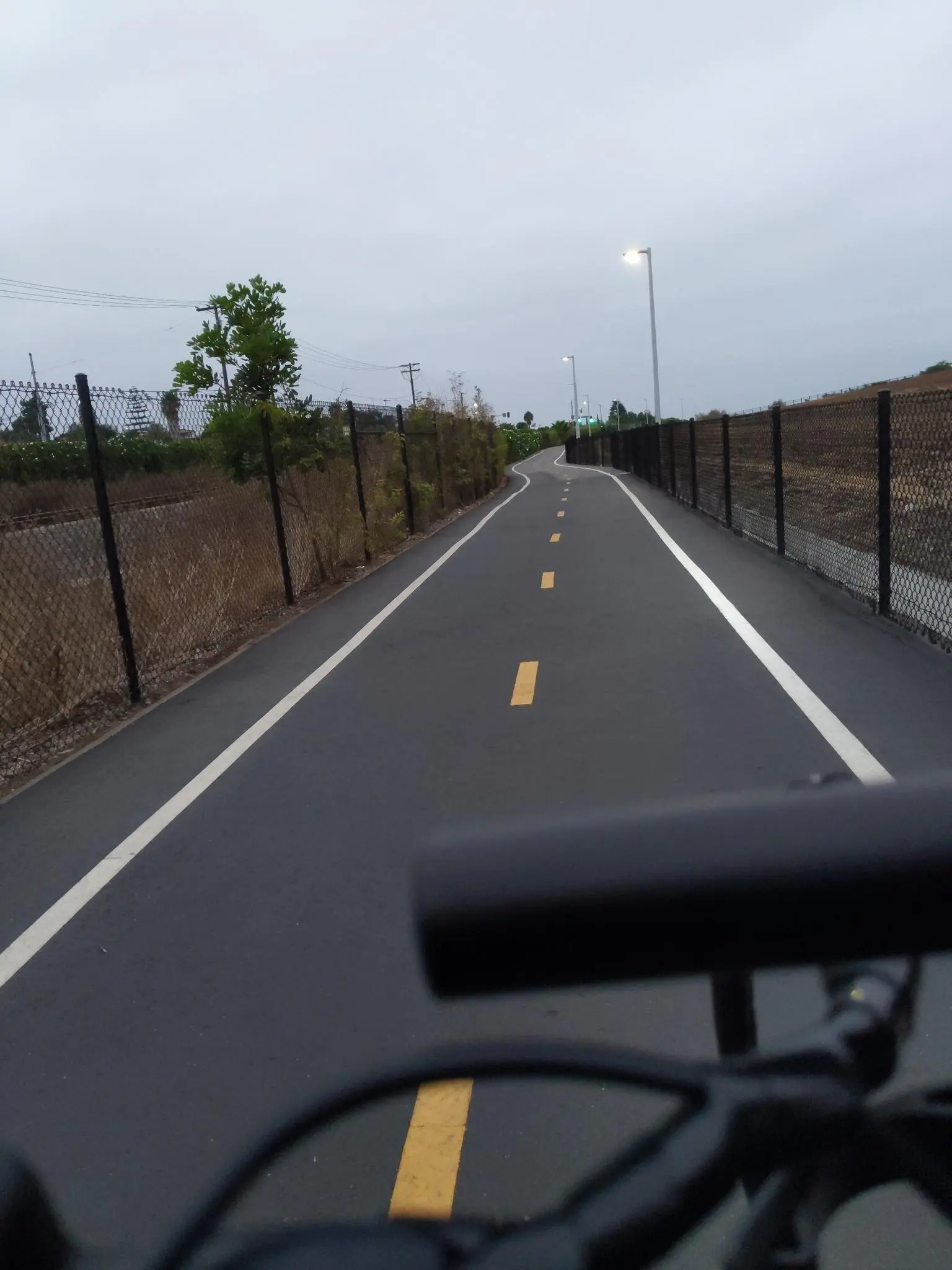 Paved bike path under an overcast sky, seen from a rider's perspective.