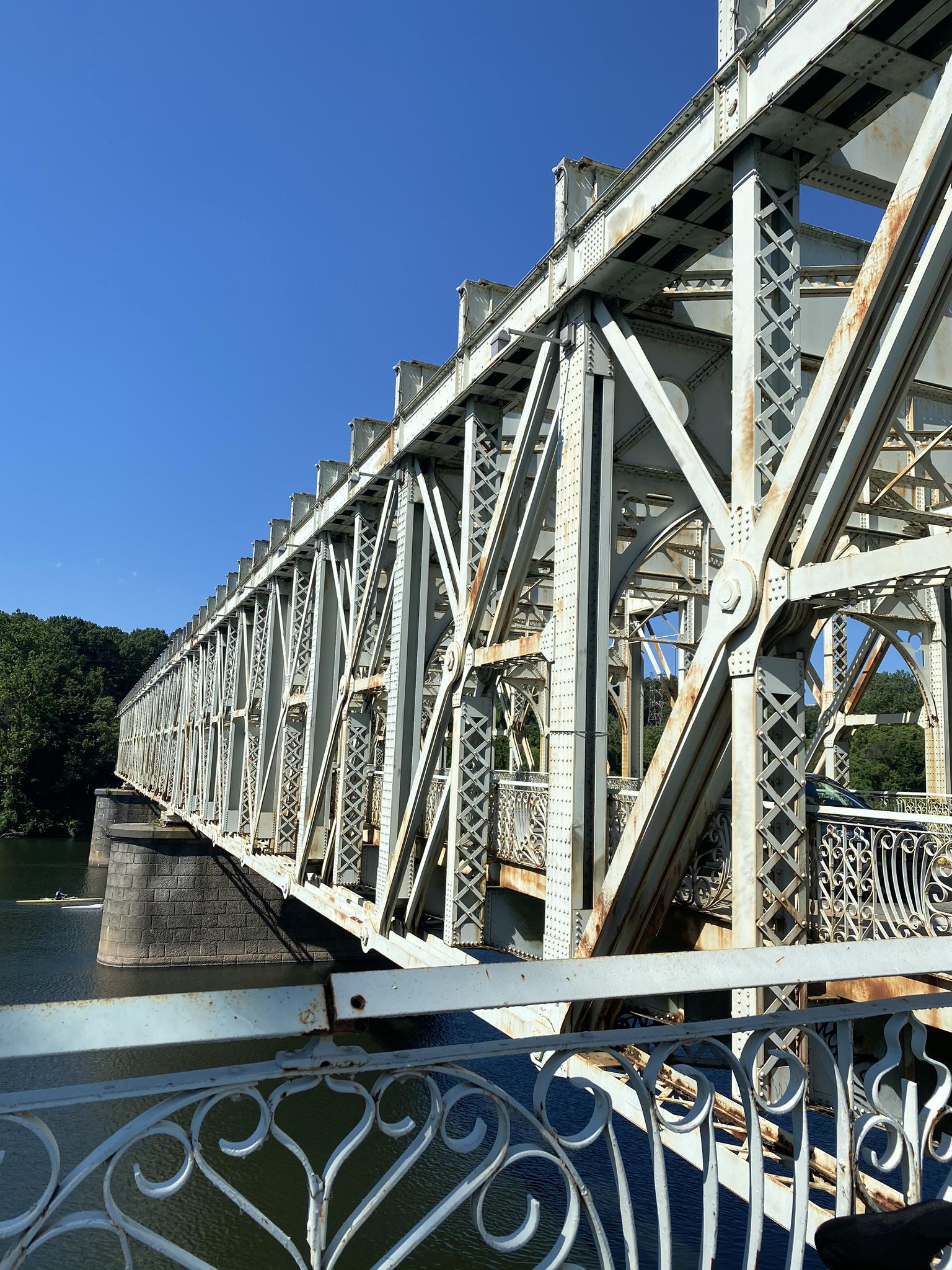 Intricate metal truss bridge spans over water under a clear blue sky.