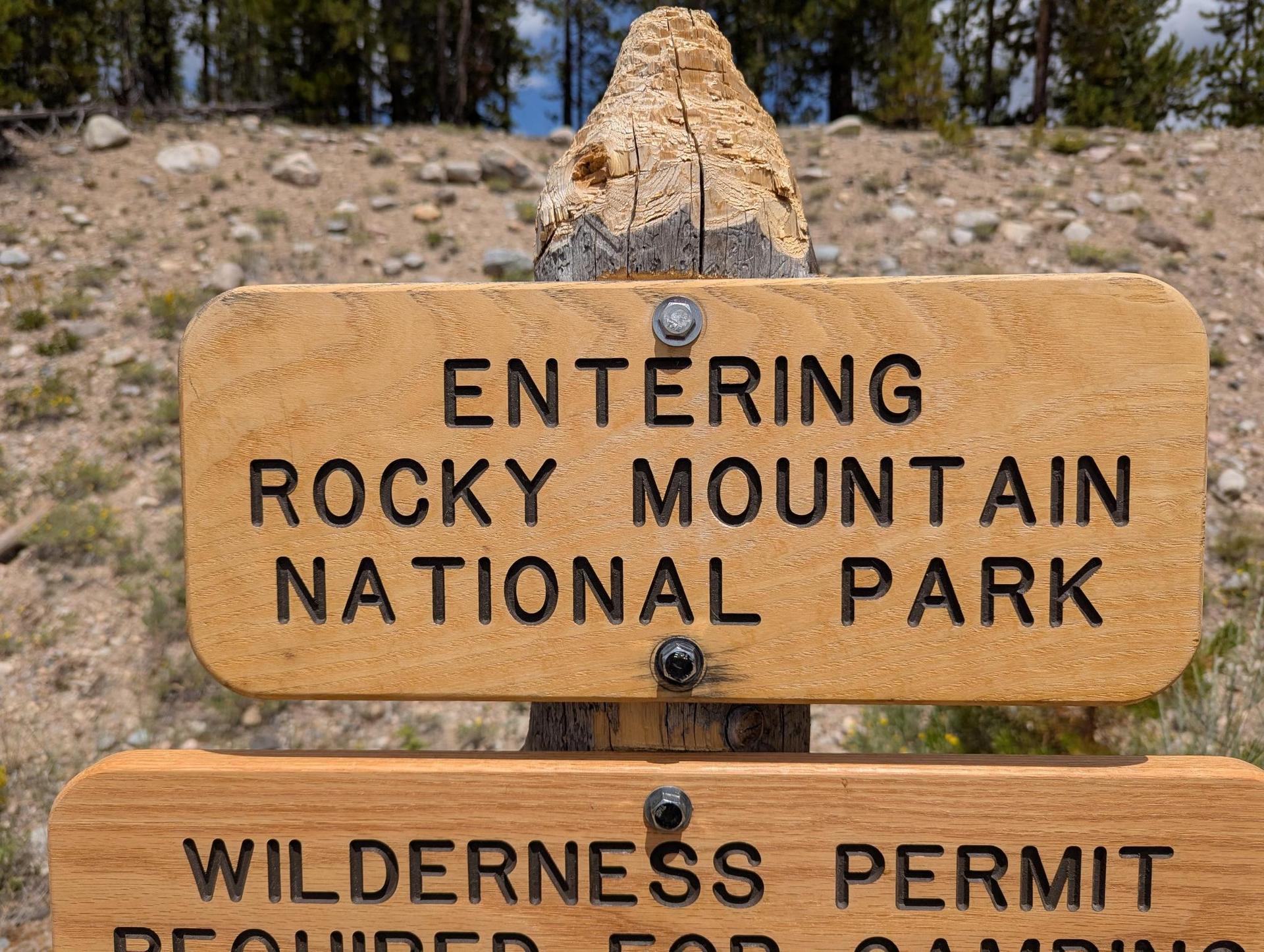 Close-up of a wooden sign with carved text, against a blurred background.