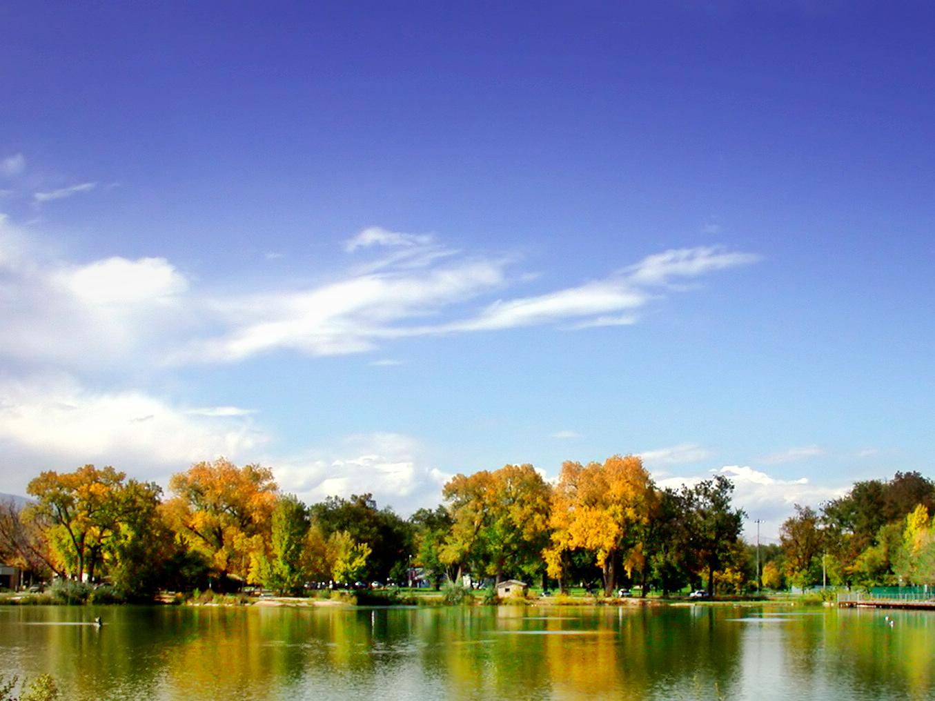 Bright sunny day over a calm lake reflecting colorful autumn trees.