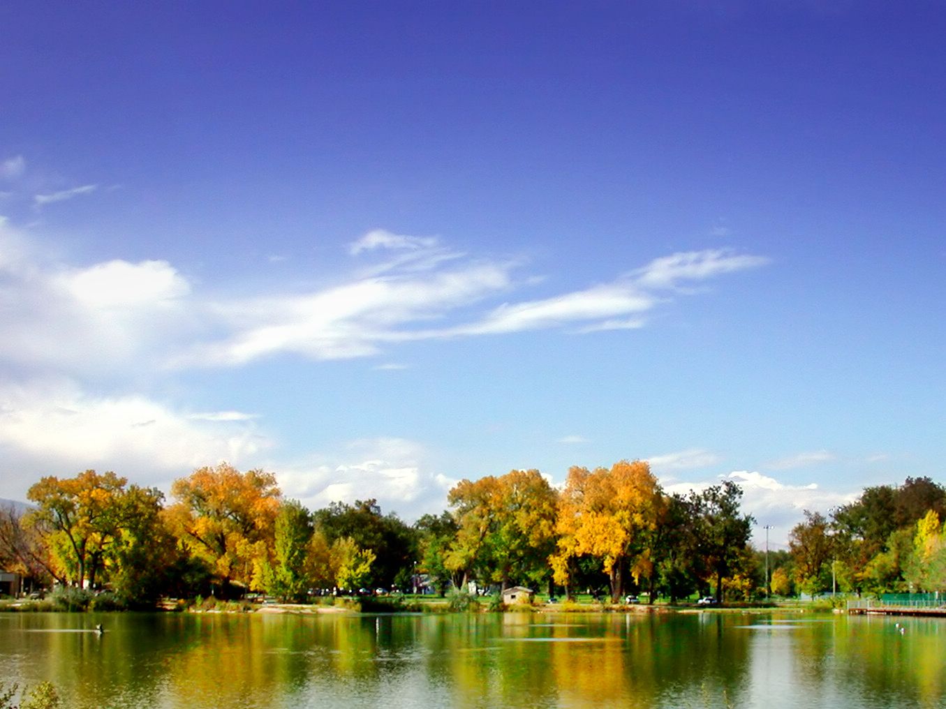 Bright sunny day over a calm lake reflecting colorful autumn trees. - Poudre River and Spring Creek Trails Loop