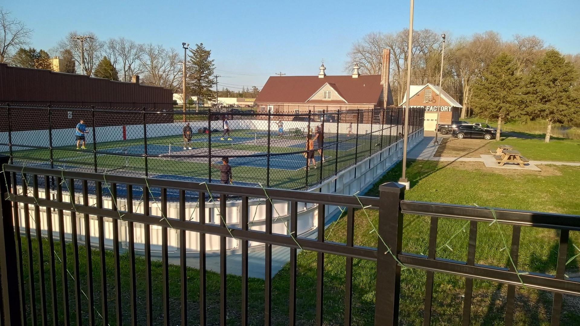 People playing on an outdoor court, surrounded by a fence, in warm light.