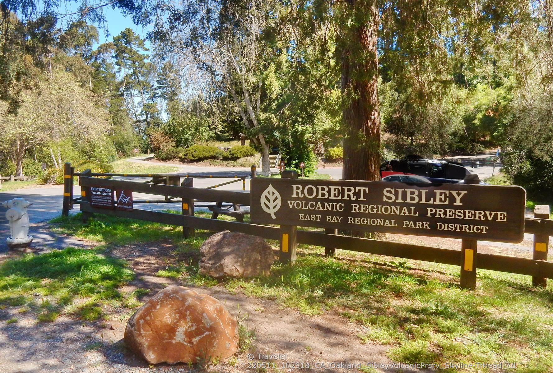 Wooden park sign and fence on a sunny day, with trees.