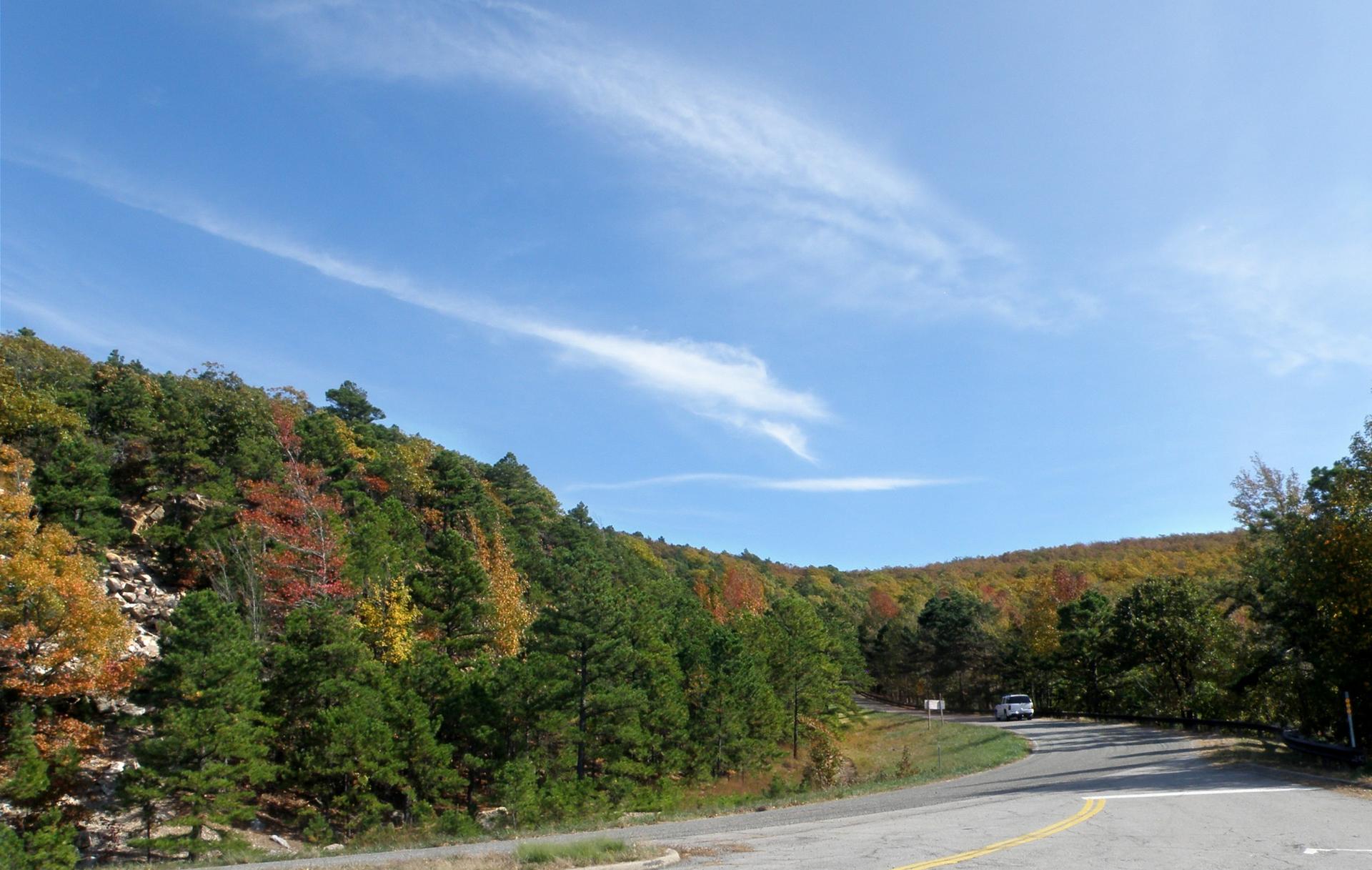 A winding road curves through a hillside of colorful autumn trees.