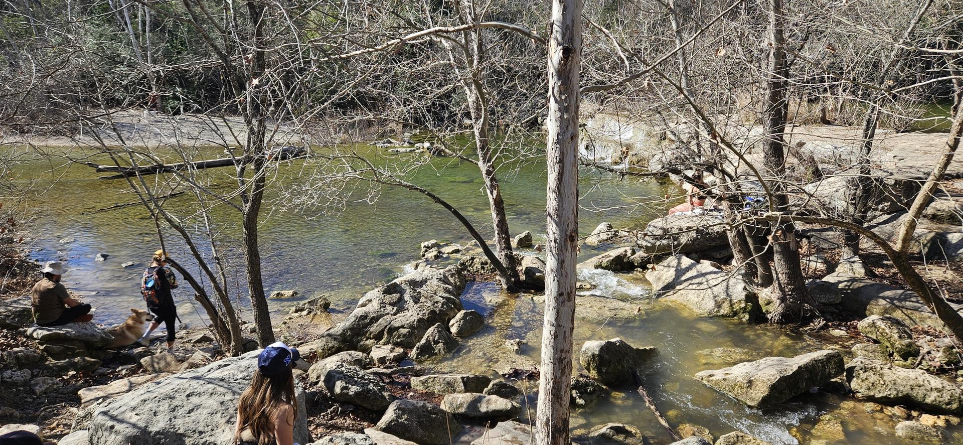People relaxing and wading in a rocky river on a bright, sunny day.