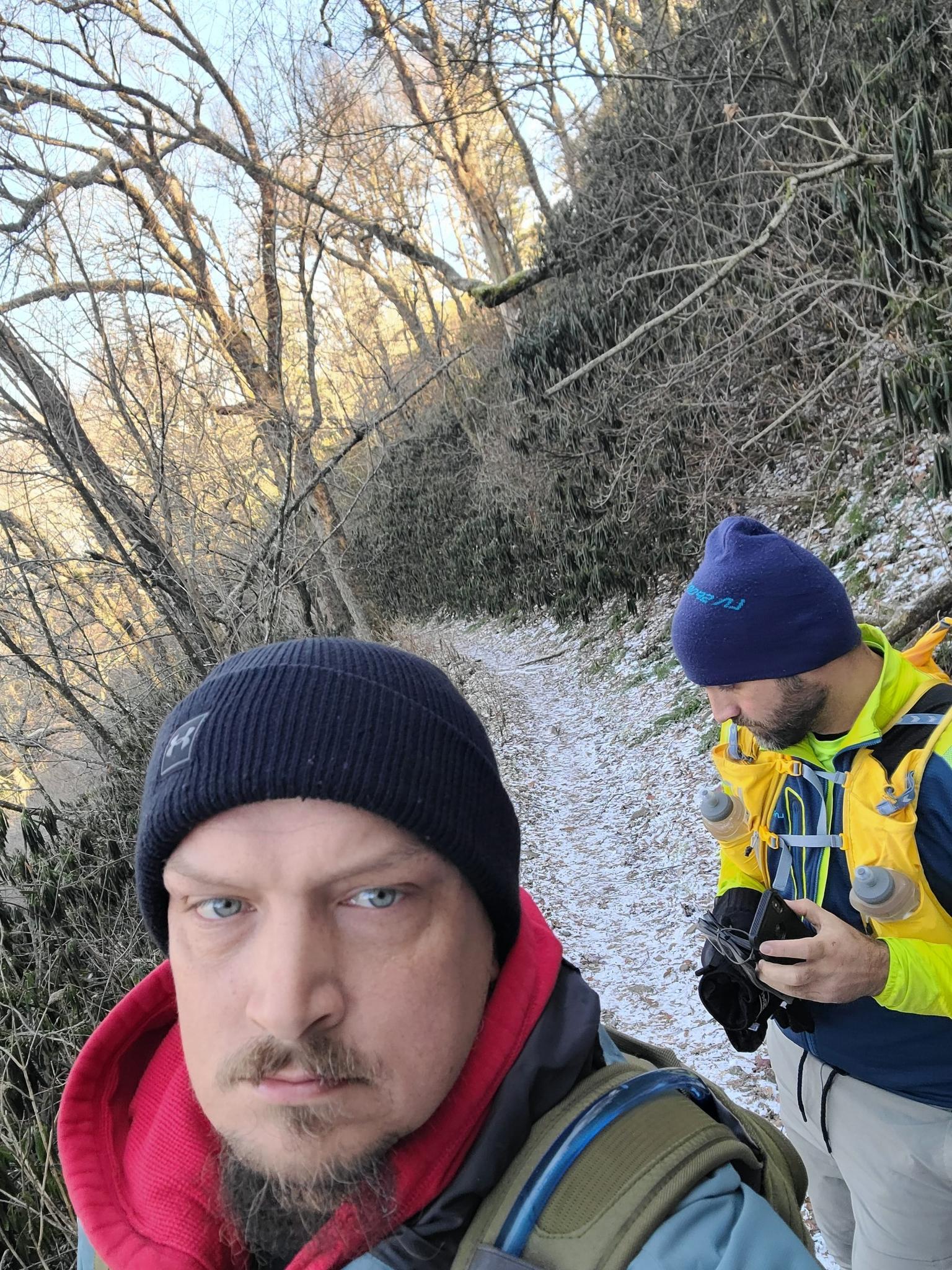Two men in beanies on a snowy path with bare trees.