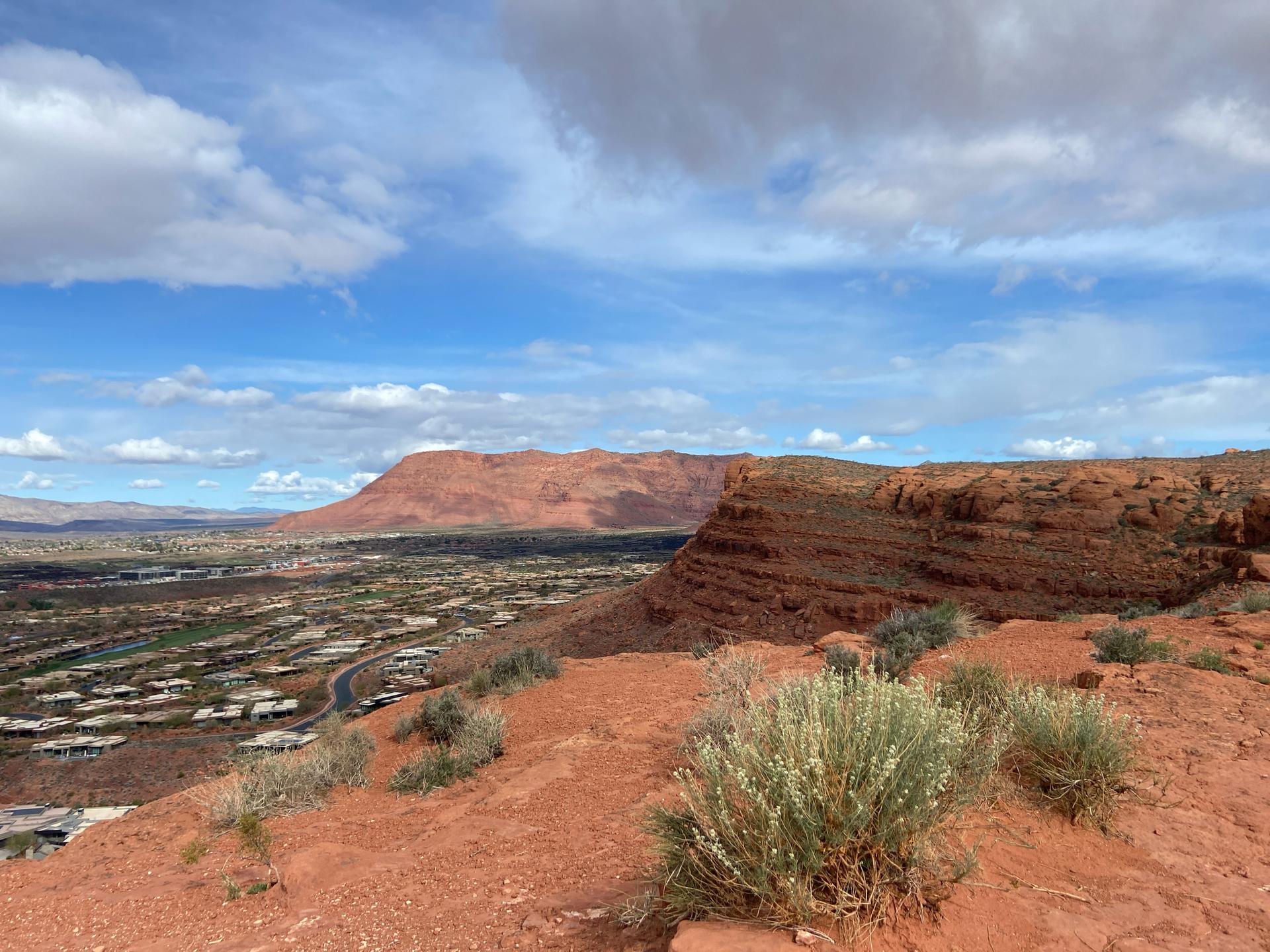 Overlook from red rock hill, showing a town and distant mountains.