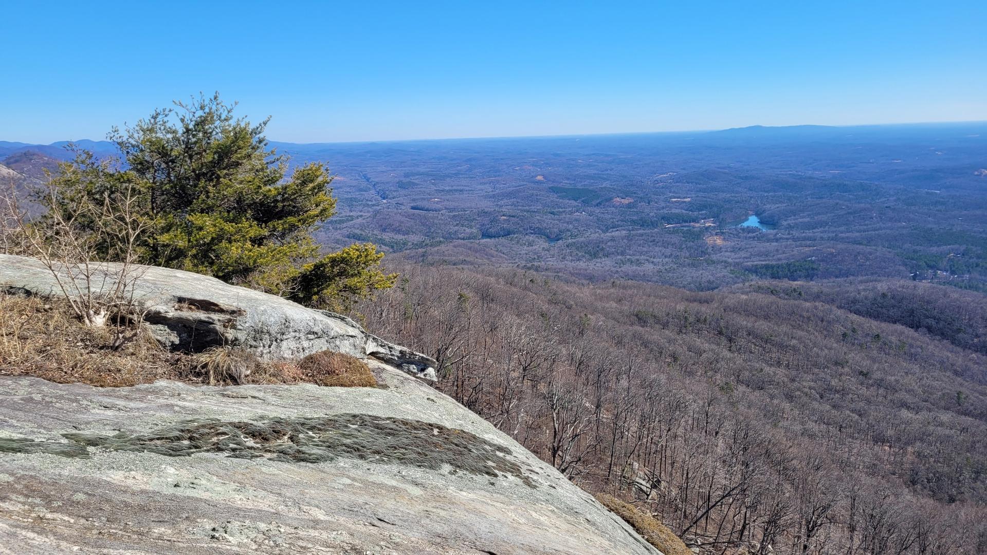 Expansive mountain vista from a rocky ledge overlooking a vast forest.