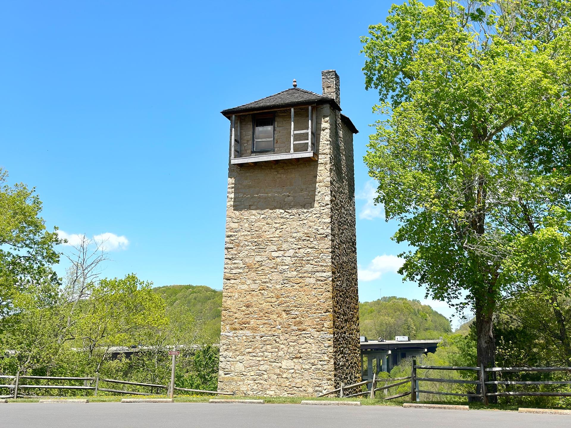 Tall stone tower with a small wooden top under a clear blue sky.