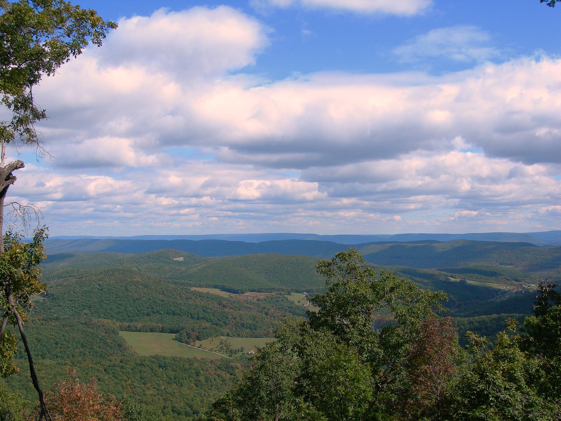 Expansive view of rolling green mountains under a bright, cloudy sky.