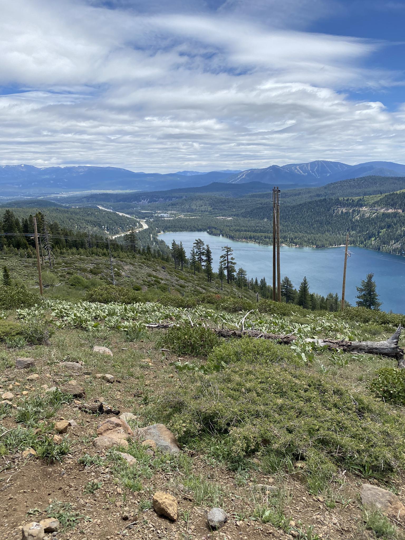 Overlook of a large lake and valley with distant mountains under a cloudy sky.