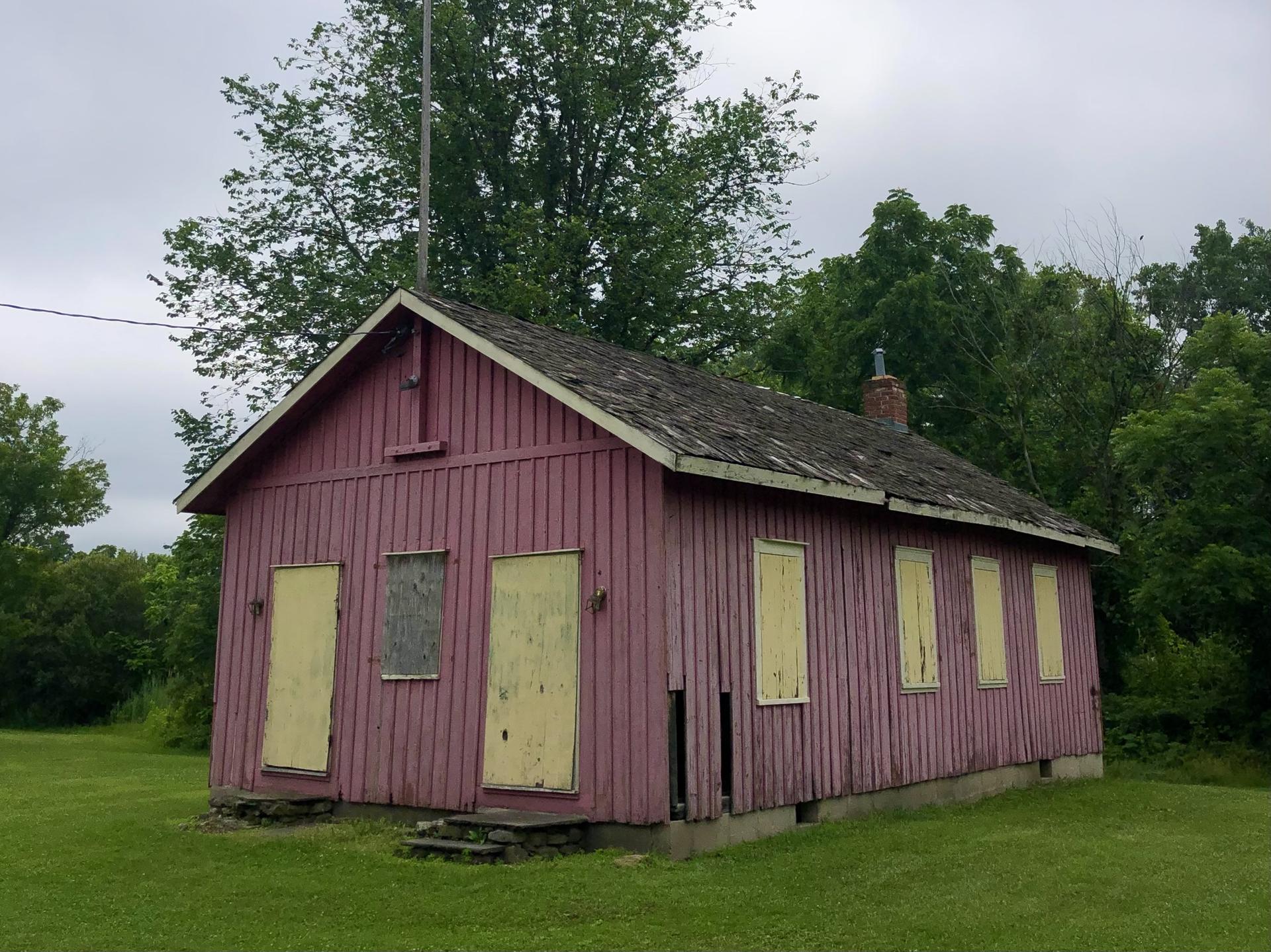 Weathered red building with yellow boarded windows in a green landscape, overcast day.