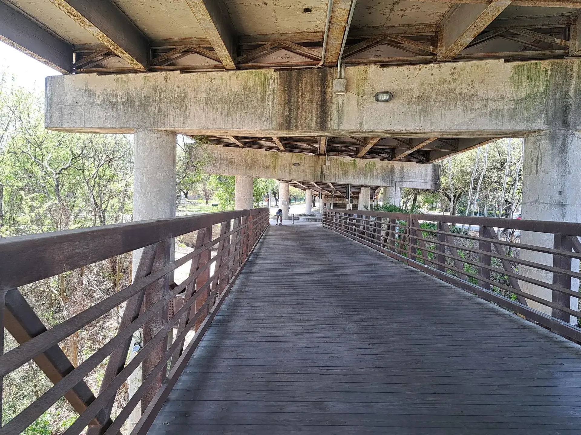 Wooden walkway under a concrete bridge with a person walking in the distance.