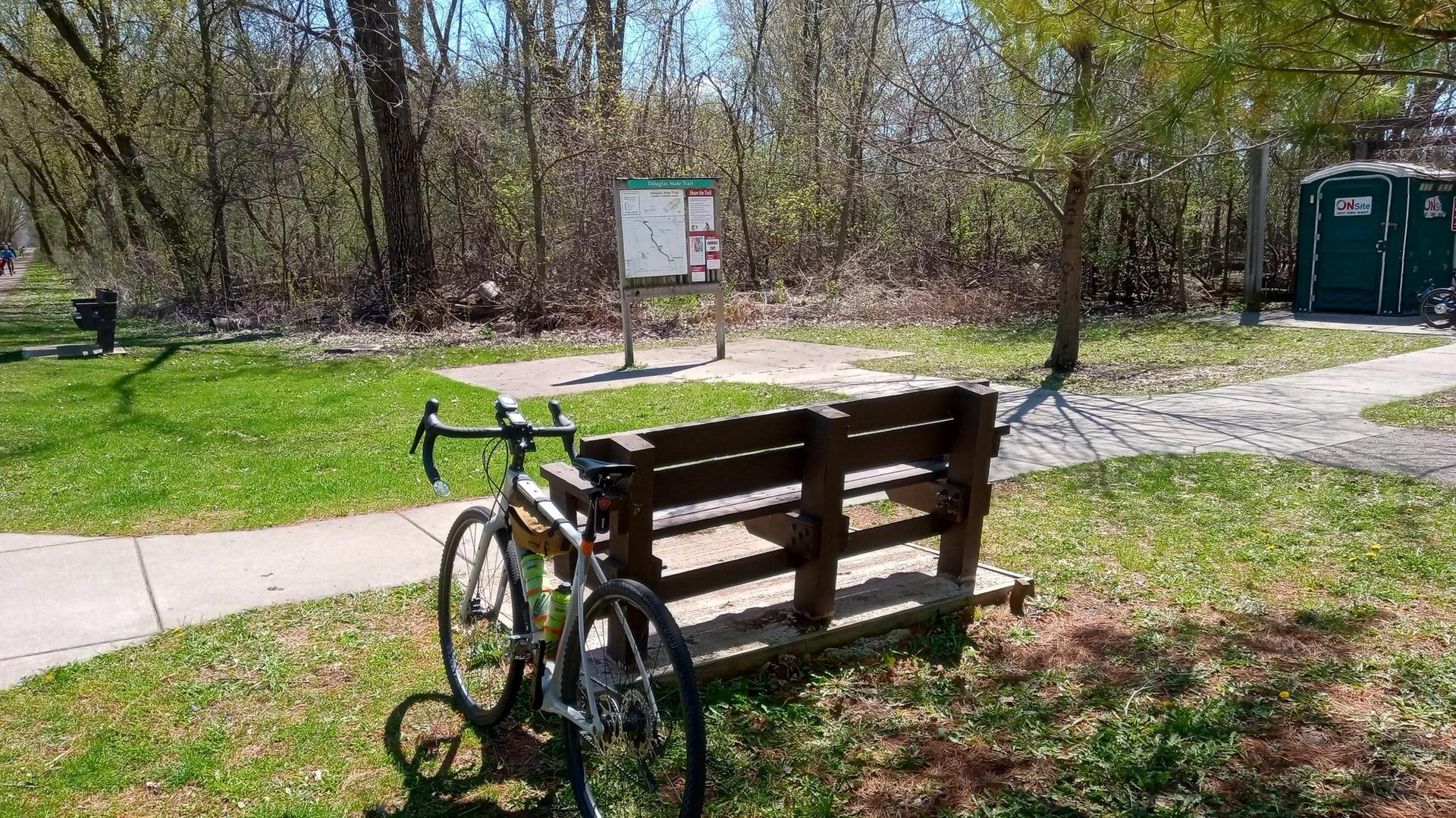 Bicycle parked next to a wooden bench on a sunny day.