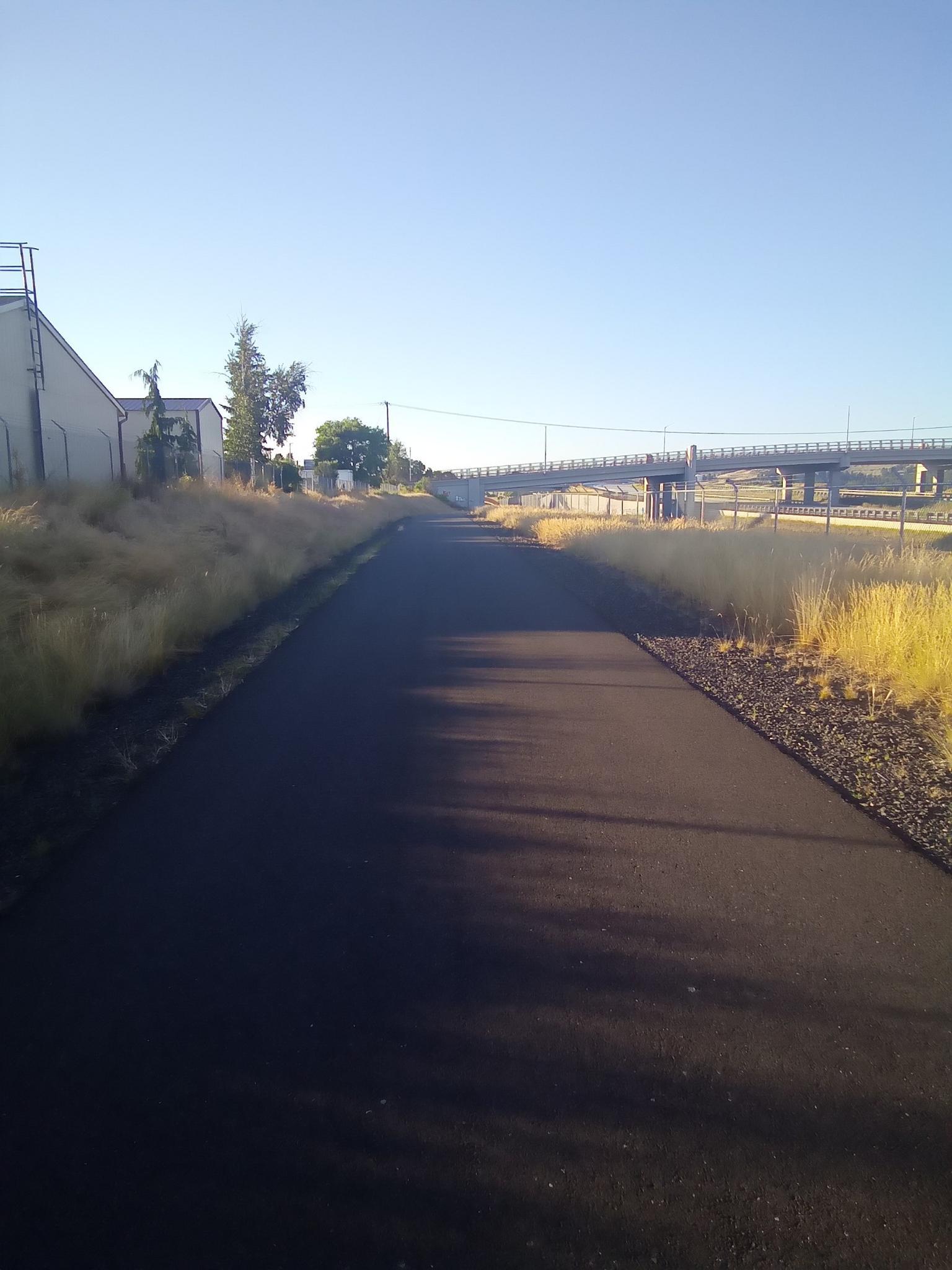 A paved path stretches through dry grass under a clear morning sky.