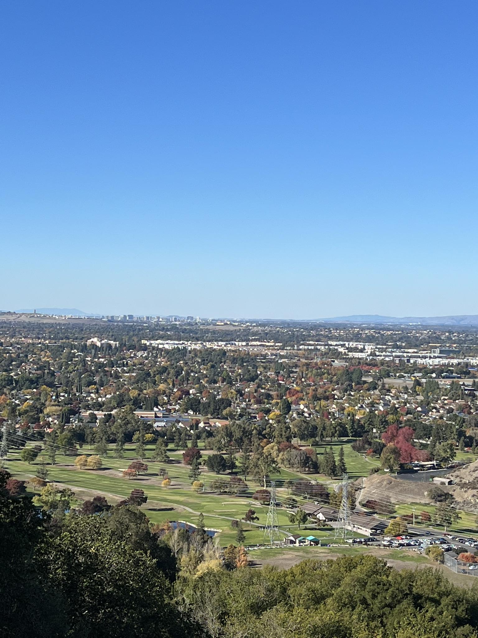 Panoramic view of a city, golf course, and distant hills on a clear day.