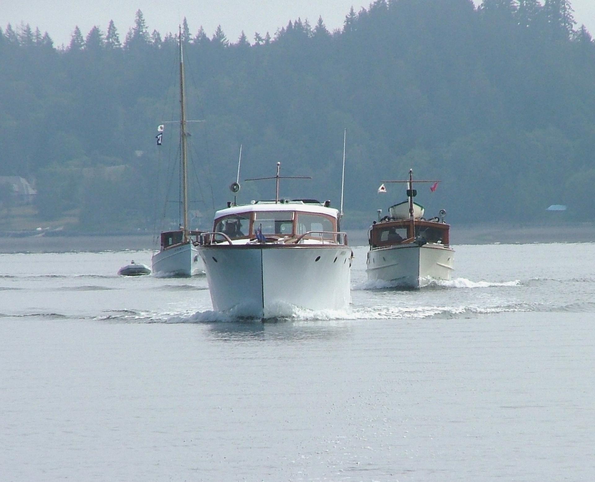 Three boats on hazy water, two motorboats leading, one sailboat behind.