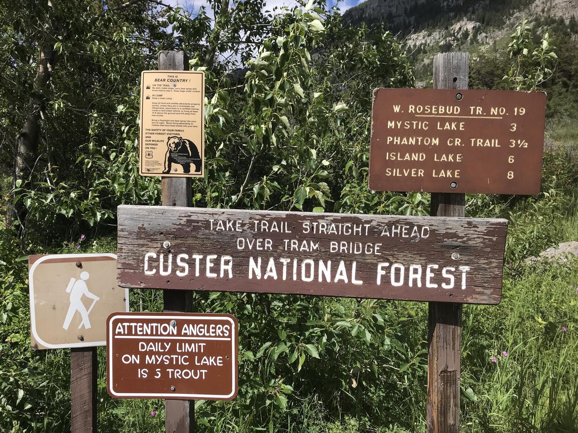 Multiple wooden trail signs with text, surrounded by green foliage.