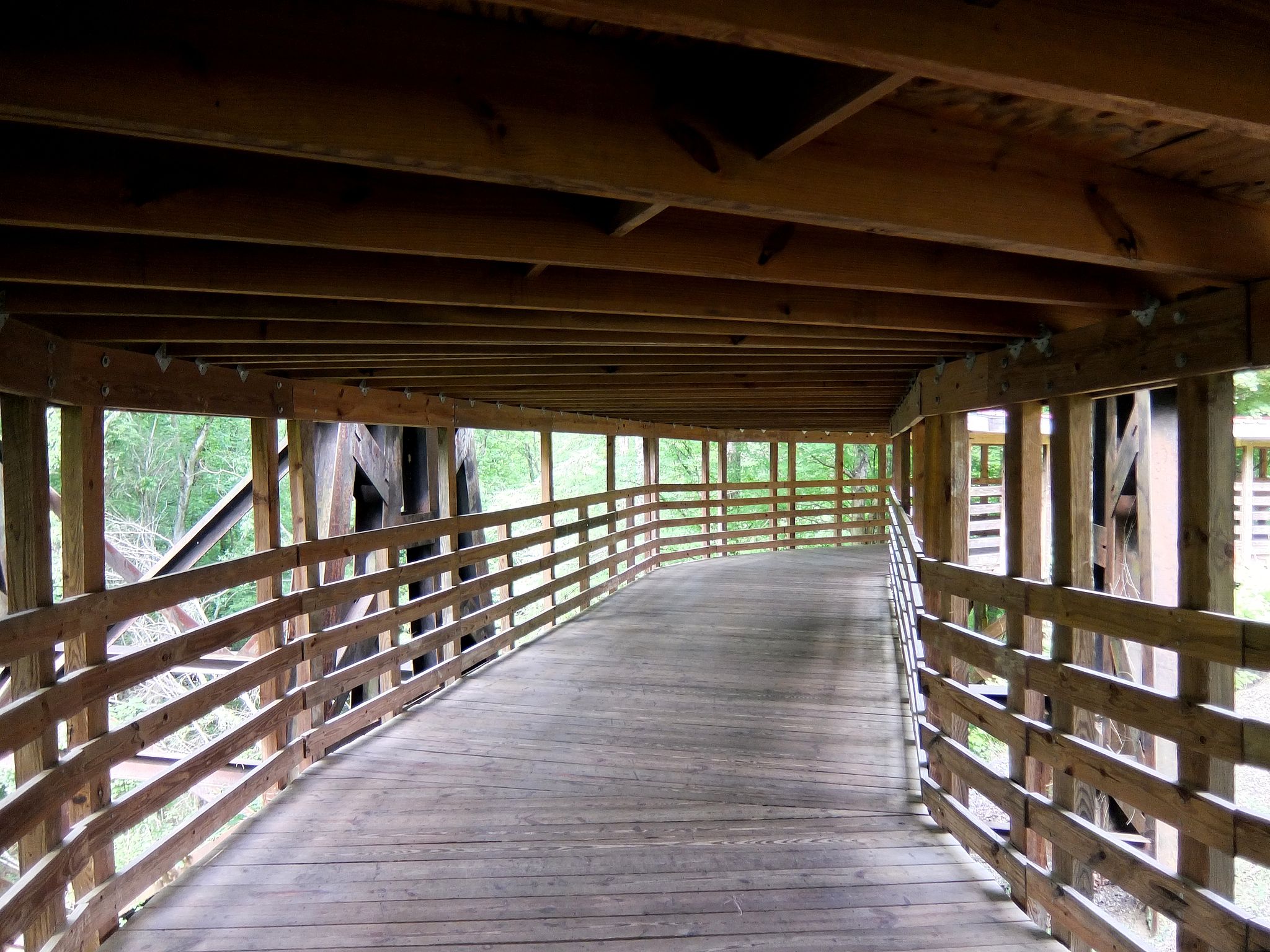 A long, empty wooden covered walkway with open sides showing green foliage. - Cape Fear River Trail