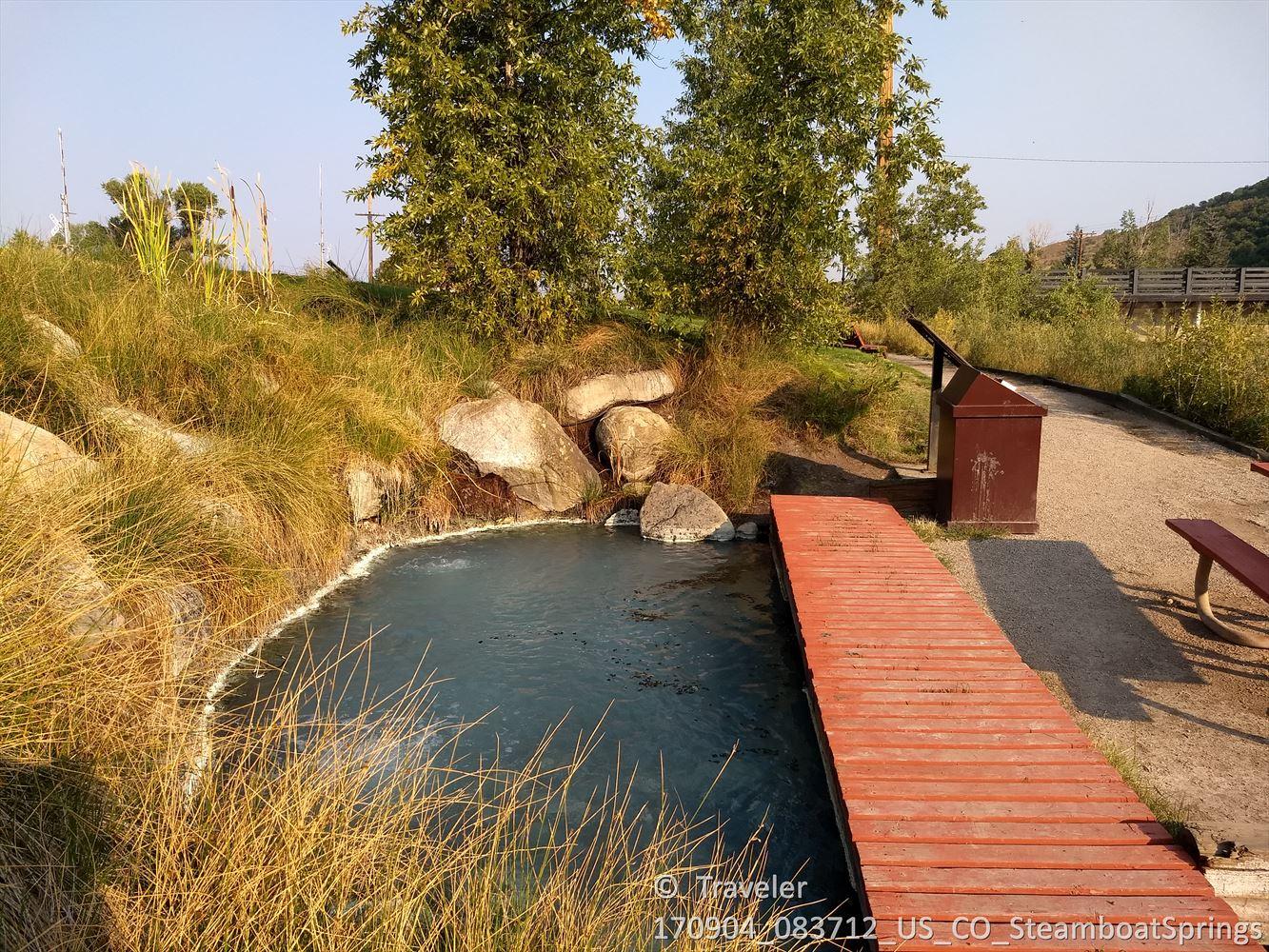 A small natural pool with a wooden boardwalk, surrounded by golden grass.