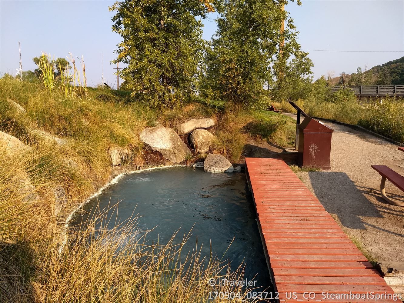 A small natural pool with a wooden boardwalk, surrounded by golden grass. - Elk Mountain loop