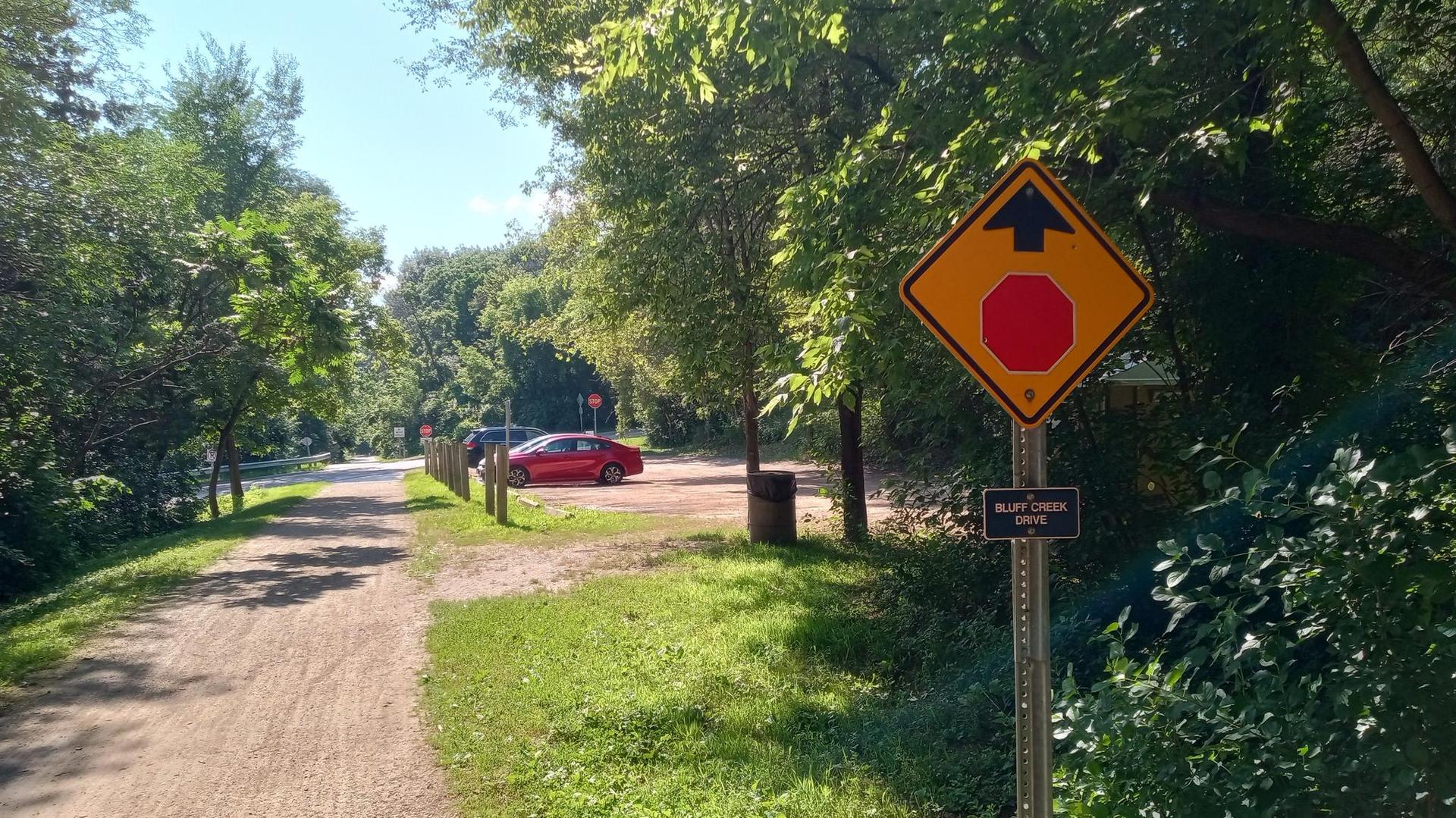 Stop sign next to a dirt path, with cars parked in the distance.