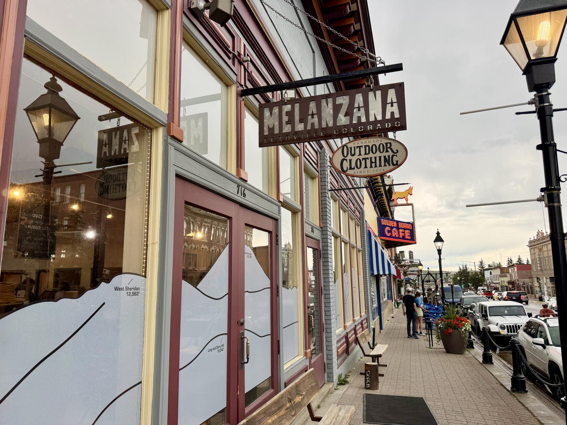 Storefronts with signs and people walking on a cloudy urban street.