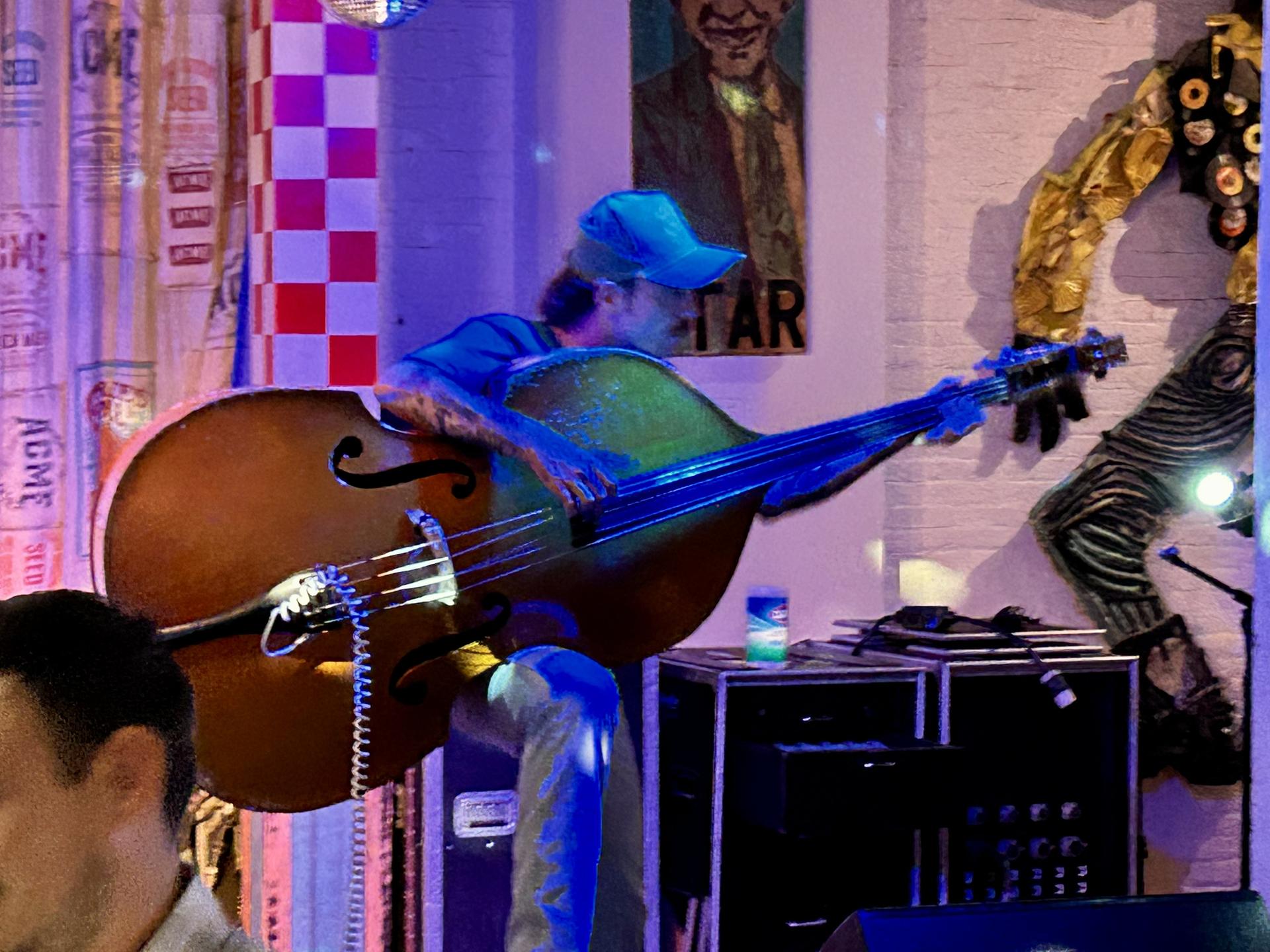 Musician playing a large upright bass on a colorful, lit stage.