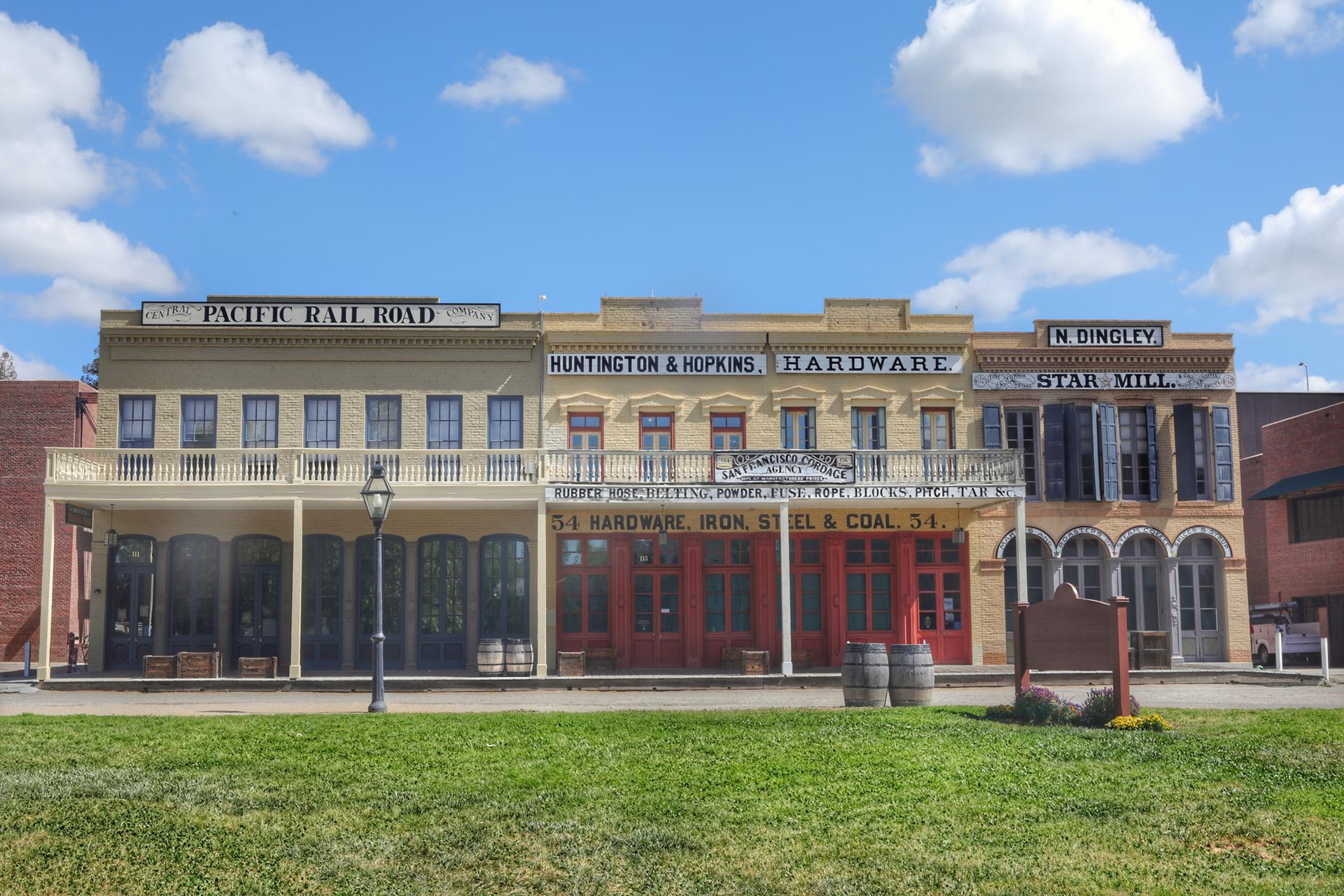 Historic storefronts with balconies, green lawn, under a blue sky.