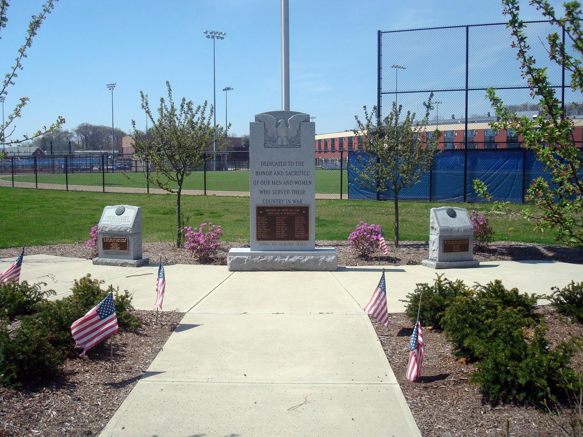 Stone monument with American flags on a sunny day near sports fields.